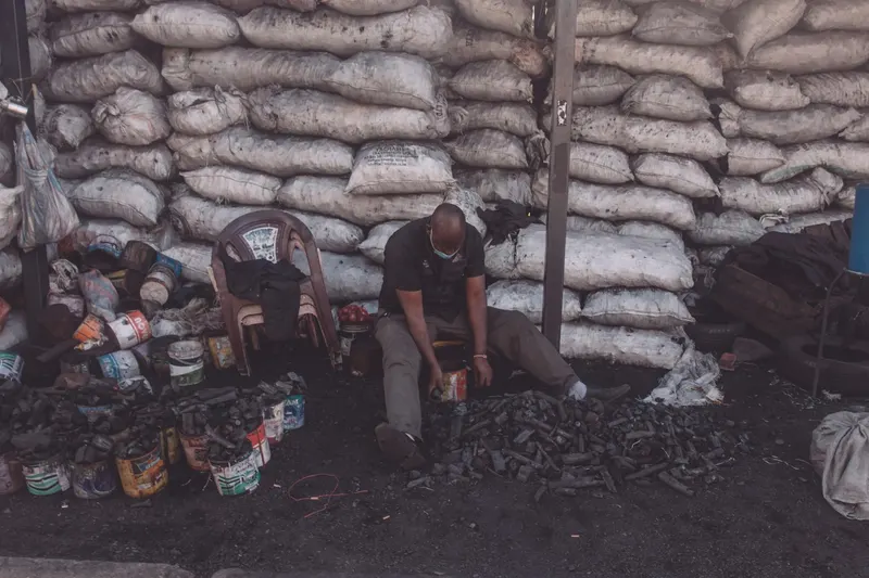 A man sitting and sorting charcoal bags in an outdoor market setting.