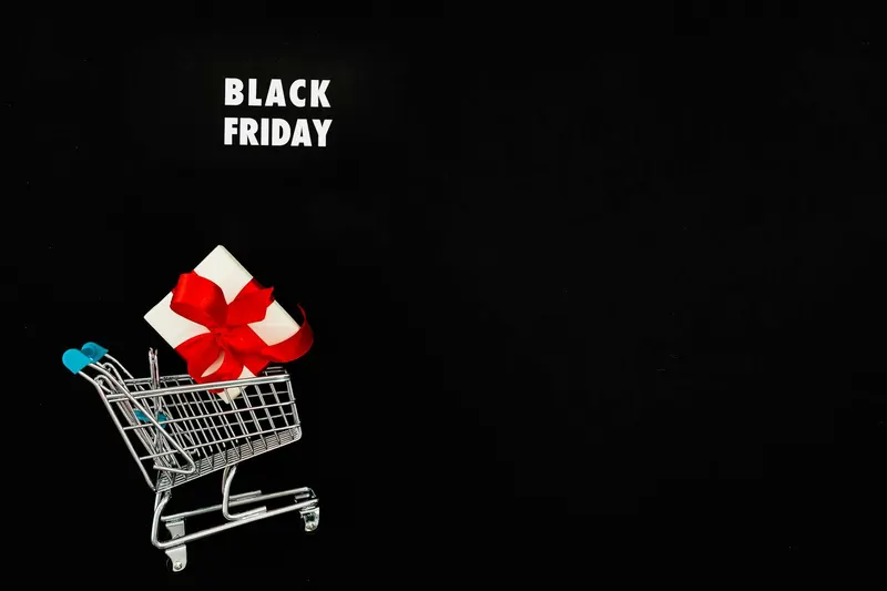Black Friday shopping concept with a gift in a mini cart against a black background, emphasizing seasonal sales.